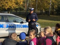 policjant opowiada dzieciom o bezpieczeństwie w tle radiowóz