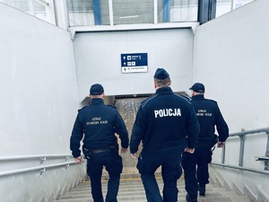 na zdjęciu policjant umundurowany schodzi po schodach z dwoma strażnikami ochrony kolei kierując się w stronę peronu