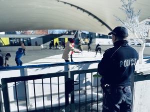 na zdjęciu umundurowany policjant obserwuje dzieci jeżdżące na lodowisku