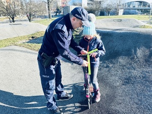 na zdjęciu umundurowany policjant zakłada dziewczynce opaskę odblaskową na hulajnogę
