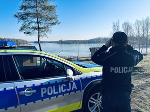 na zdjęciu umundurowany policjant obserwuje przez lornetkę zamarznięty zalew Sosina