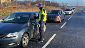na zdjęciu umundurowany policjant ruchu drogowego dokonuje pomiaru za zawartość alkoholu u kierowcy