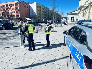na zdjęciu dwóch nieumundurowanych policjantów stojących przy przejściu dla pieszych, którzy rozmawiają z kobietą z dzieckiem.